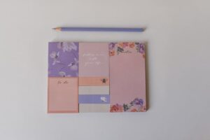 A top view of colorful sticky notes with floral designs and a purple pencil on a white background.